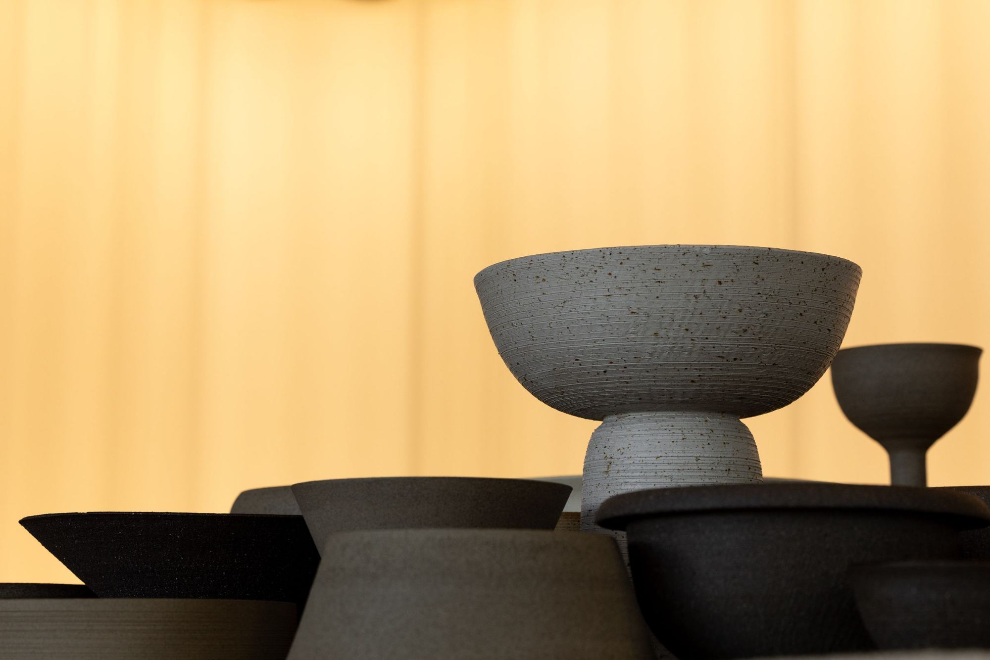 Dark handmade bowls in silhouette against a golden curtain